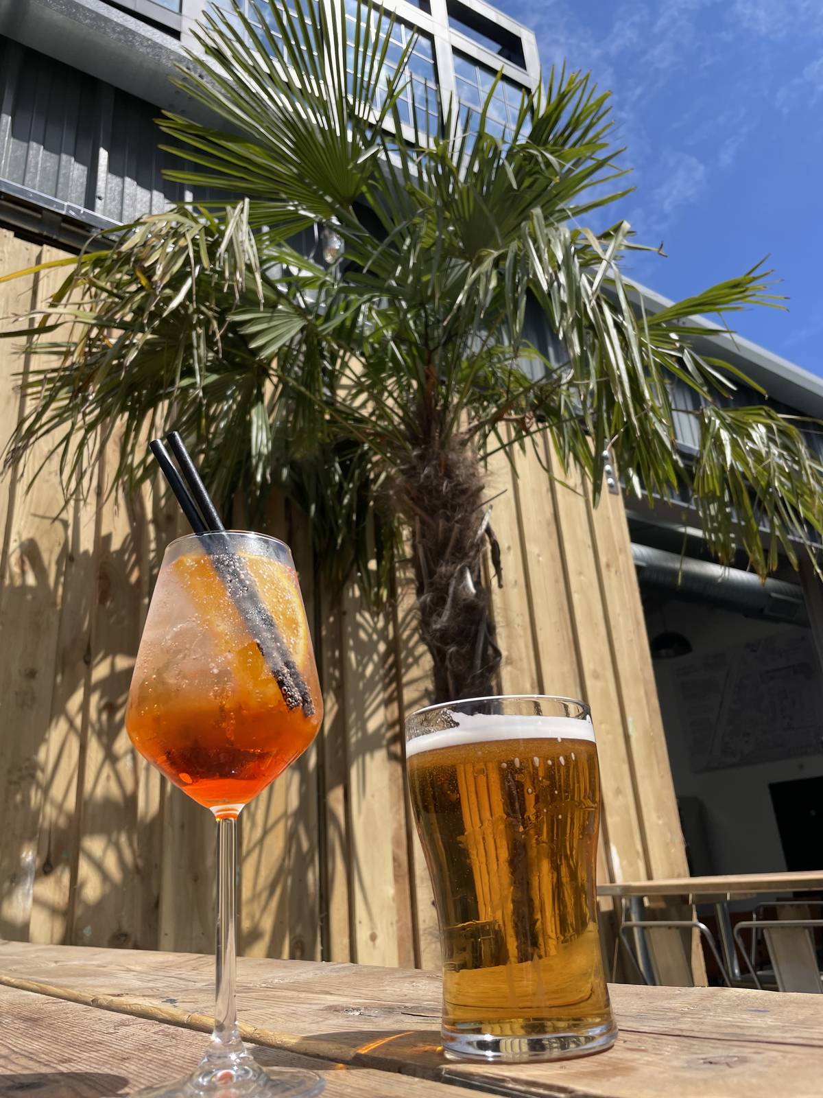 aperol spritz and pint of beer on table in front of palm tree at courts club manchester