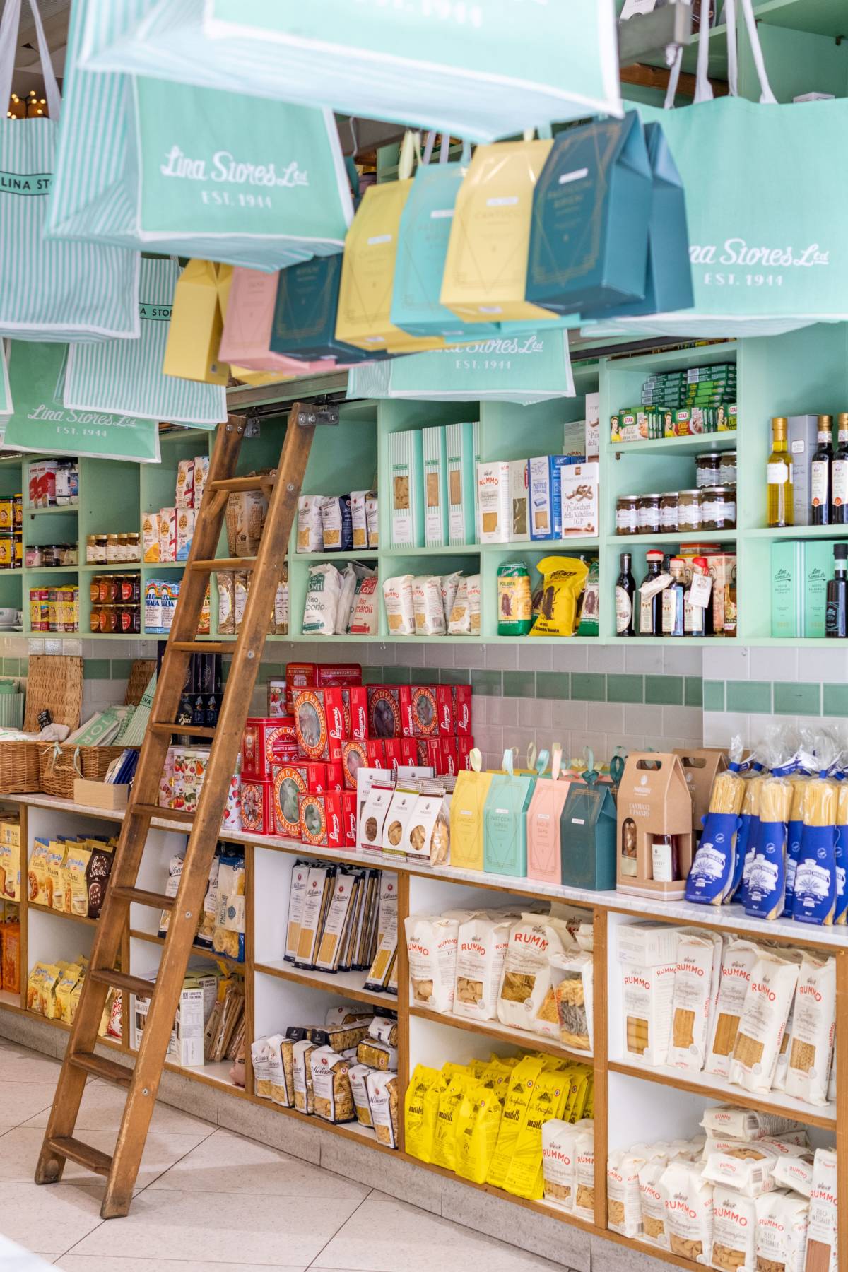 interior of deli on Brewer Street with shelves and ladder and shopping bags hanging from ceiling