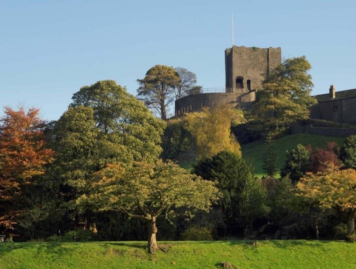 clitheroe castle from below with autumnal trees and grass in front