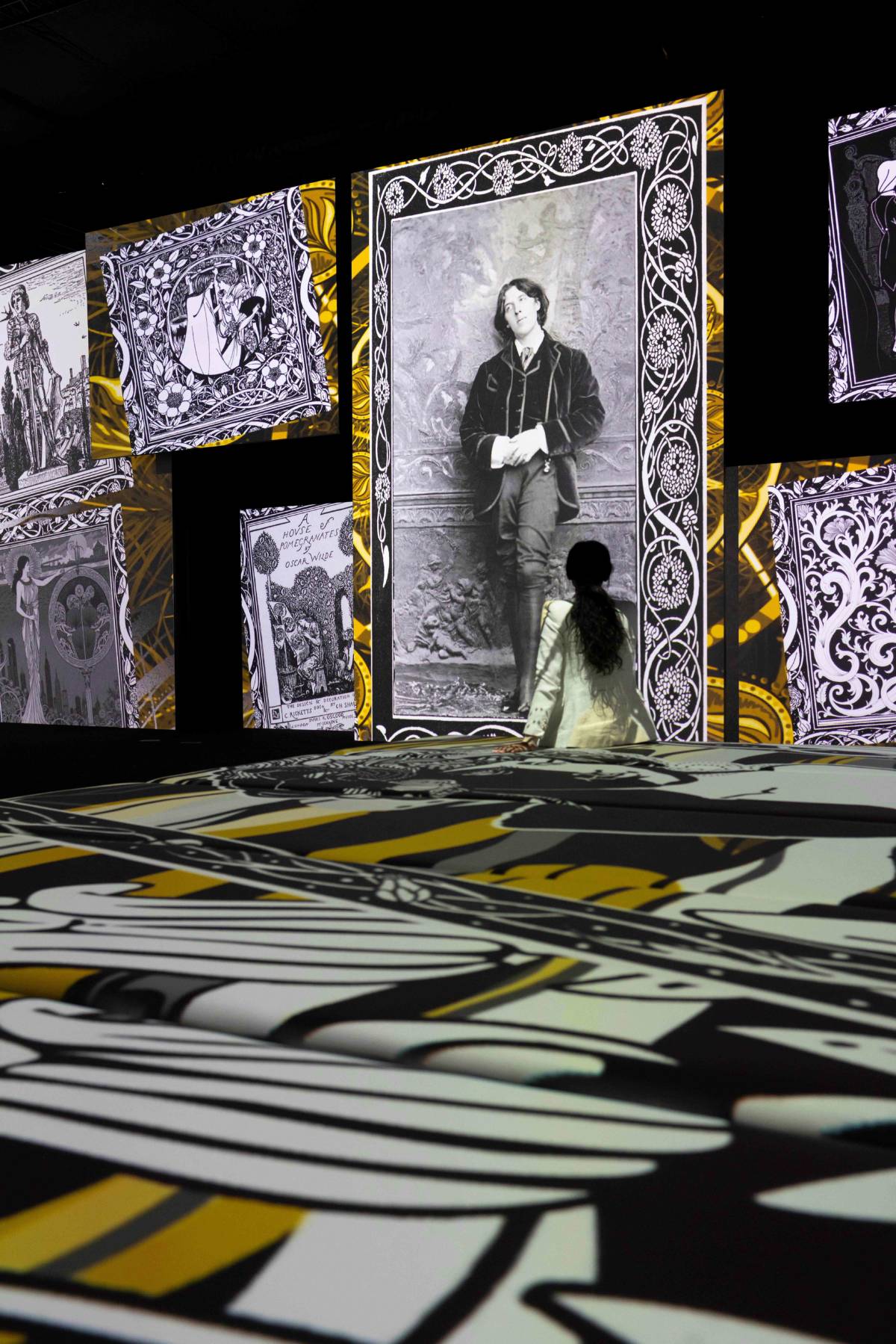 person sat on ground at immersive exhibition 'stories brought to life' with projects of portraits of Oscar Wilde on floors and walls