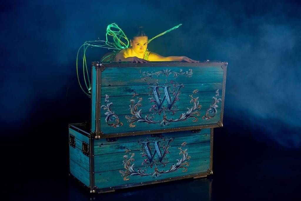 A ballerina dressed in a sparkling Tinker Bell costume hiding behind a treasure chest