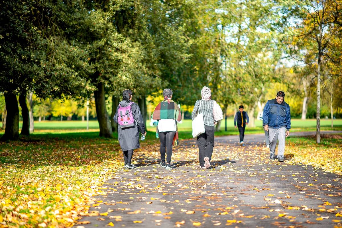 group of people walking in park with leaves on ground