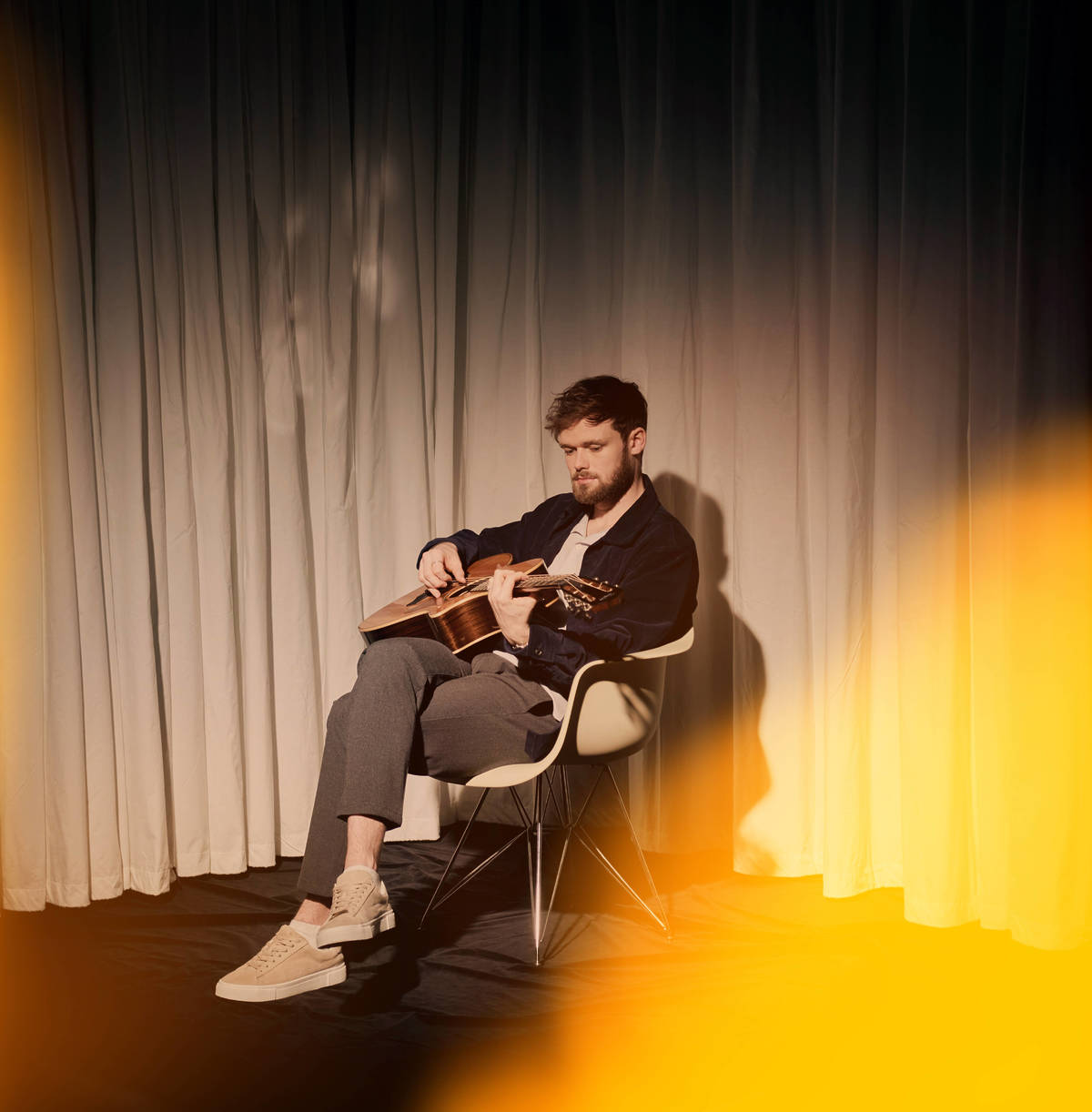 James TW playing a guitar under a golden glow.