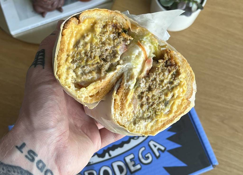 cross section of chopped cheese sub in hand above brodega shoe box