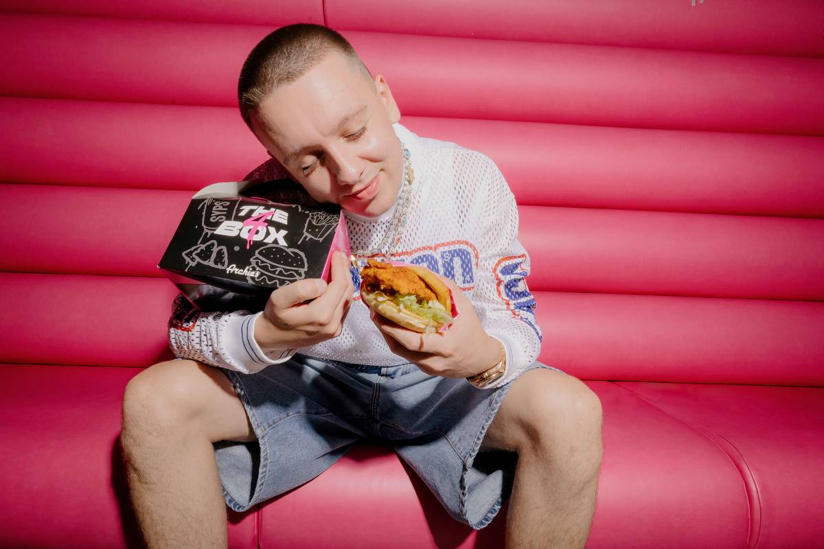 Aitch holding box and burger sat on pink booth seat