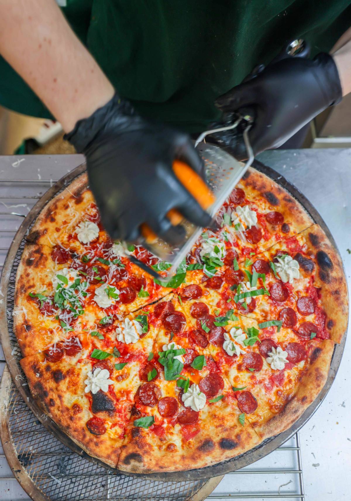 person grating cheese over giant pepperoni pizza, which Dough religion is giving free slices of this week