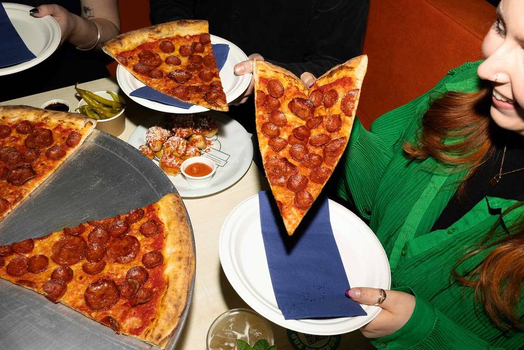 people eating slices of pepperoni pizza at nell's