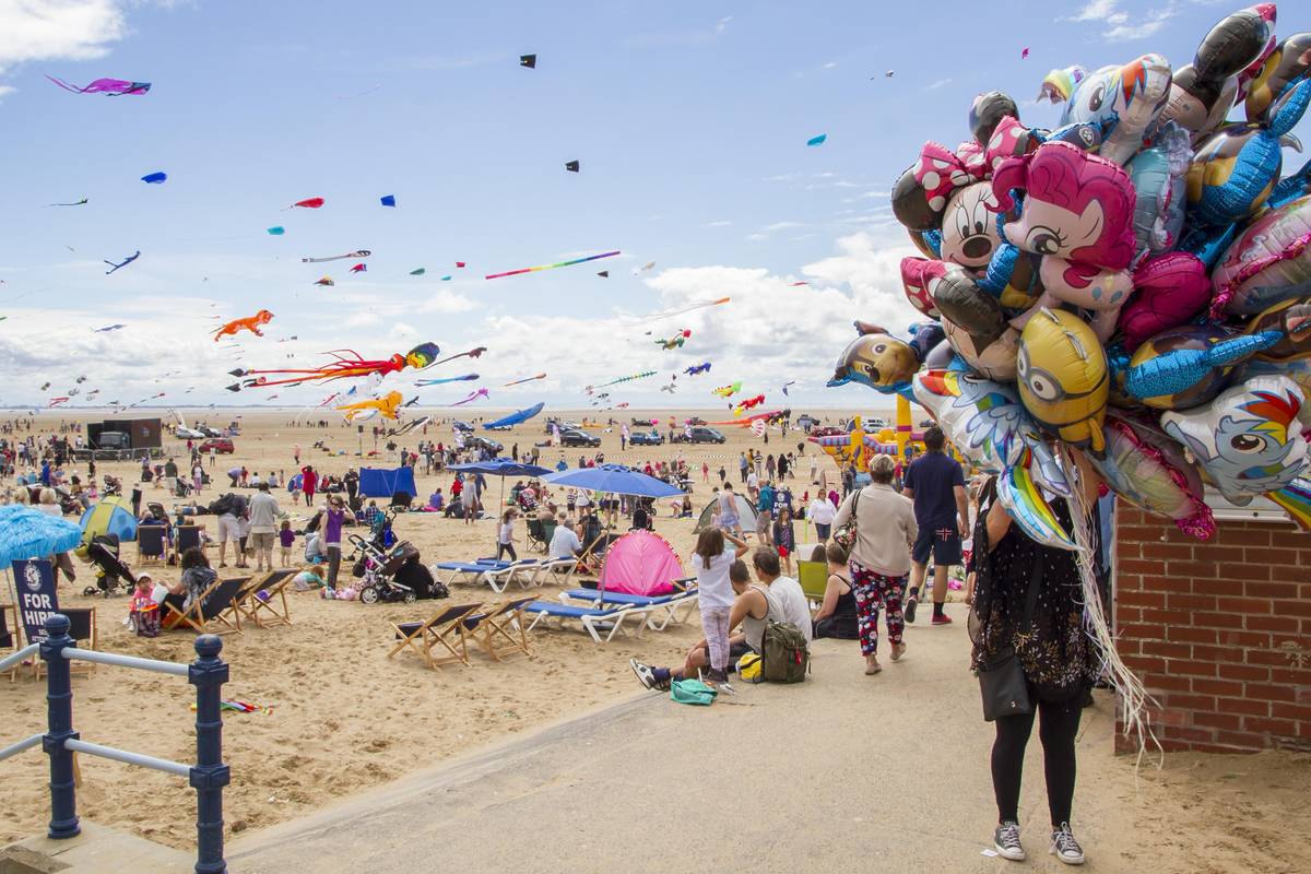 woman holding bunch of balloons next to kite festival on st annes beach
