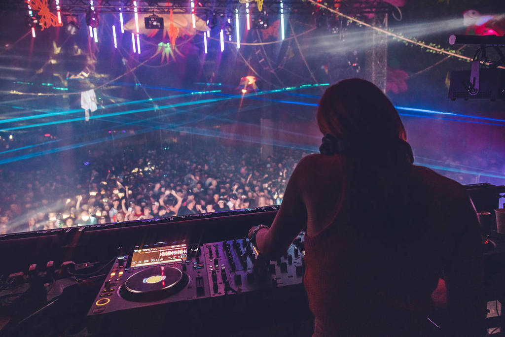 the back of a DJ performing in front of a crowd with lasers and decor above them