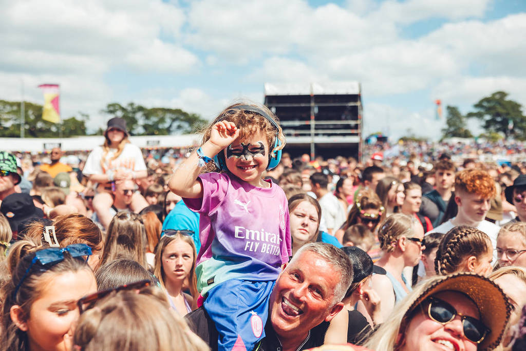 a child with face paint on the shoulders of her dad at a festival