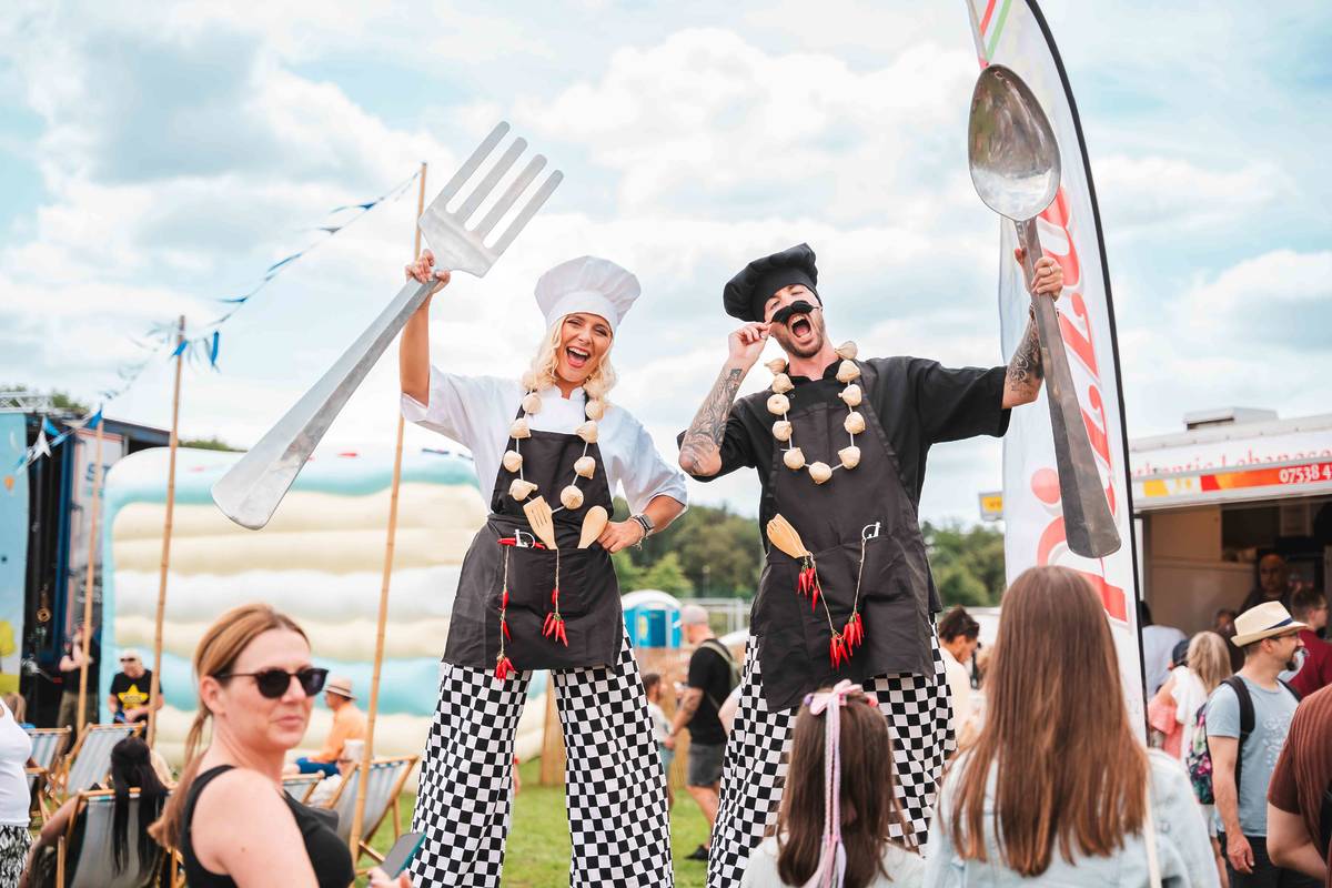 man and women dressed as chefs on stilts with giant fork and spoon