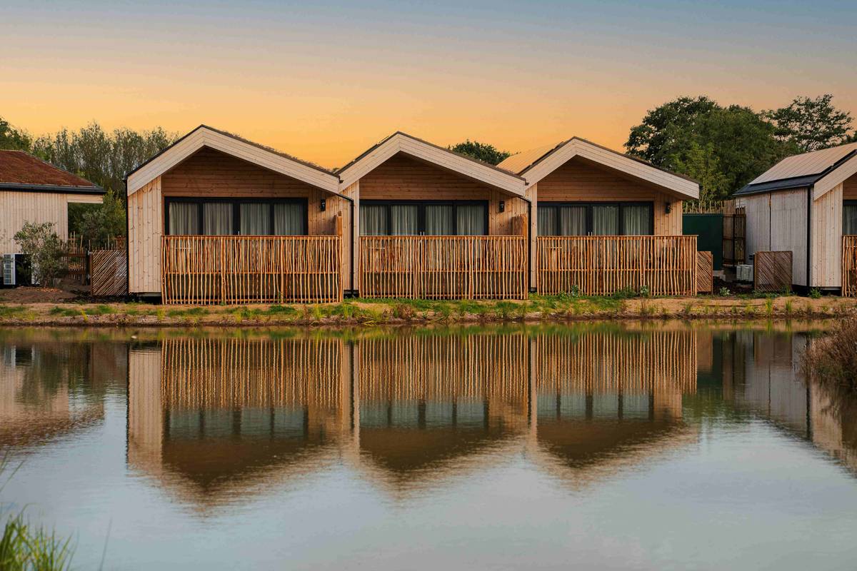 three safari-style lodges in a row reflecting on the water of the lake