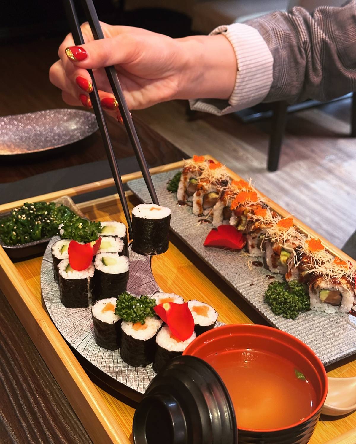 person taking maki roll with chopsticks at sushi mami