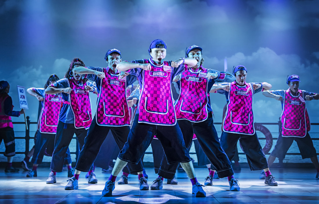 cast of here & now dancing on stage with pink tabards