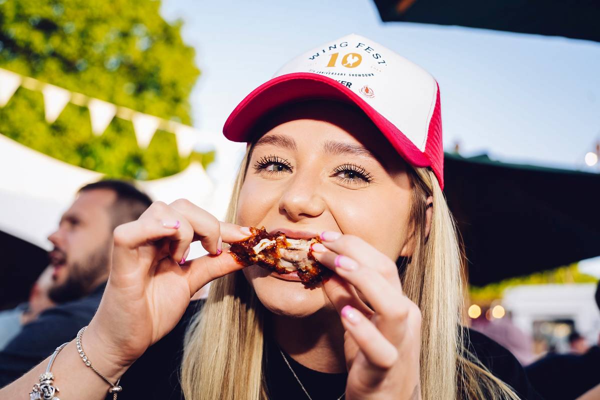 women eating chicken wing wearing trucker hat at wing fest