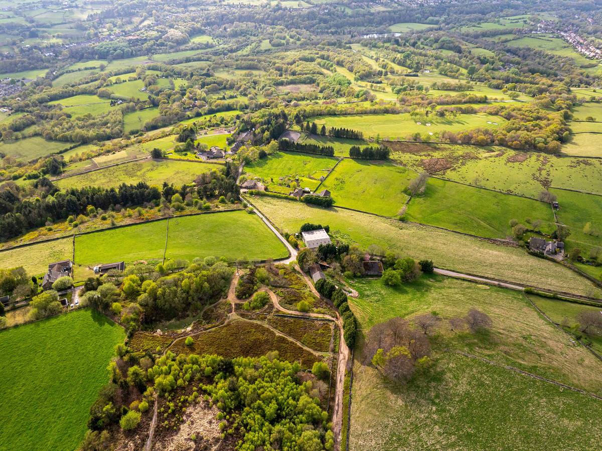 Panoramic aerial image of a countryside landscape near New Mills, in UK featuring green fields and farmlands.