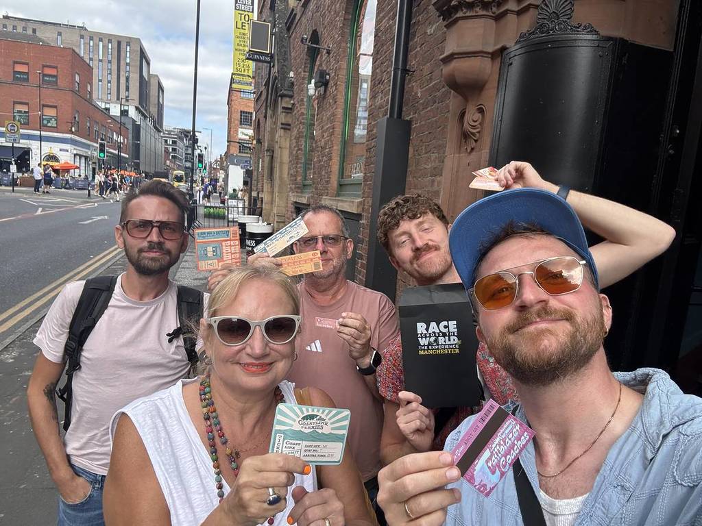 a group of people take a selfie as they hold up Race Across The World pamphlets and game tickets