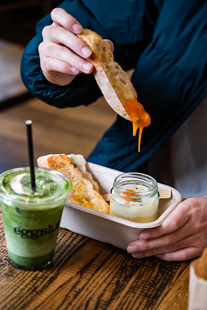 person dipping toast into coddled eggs pot next to iced matcha drink