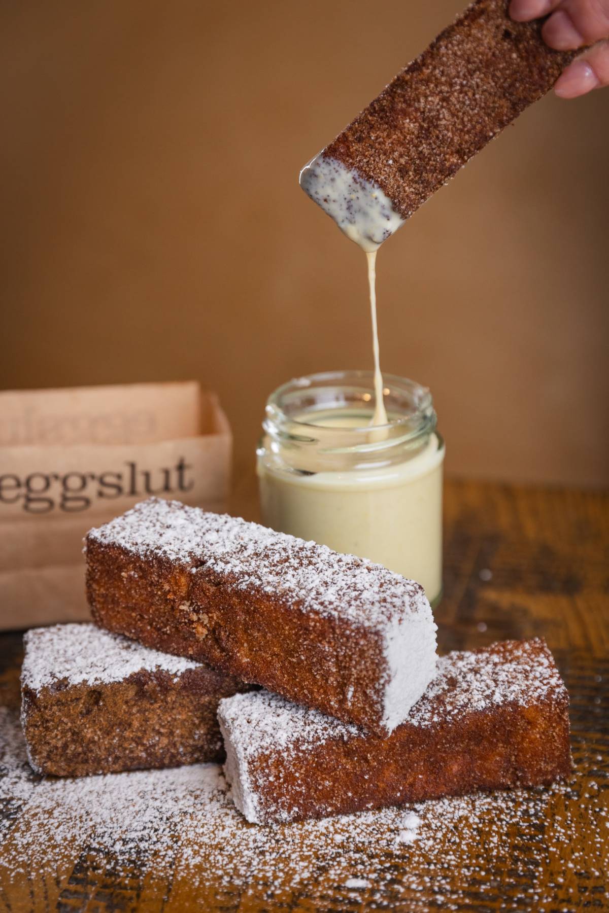 french toast sticks with dusting of icing sugar with one being dipped into maple custard