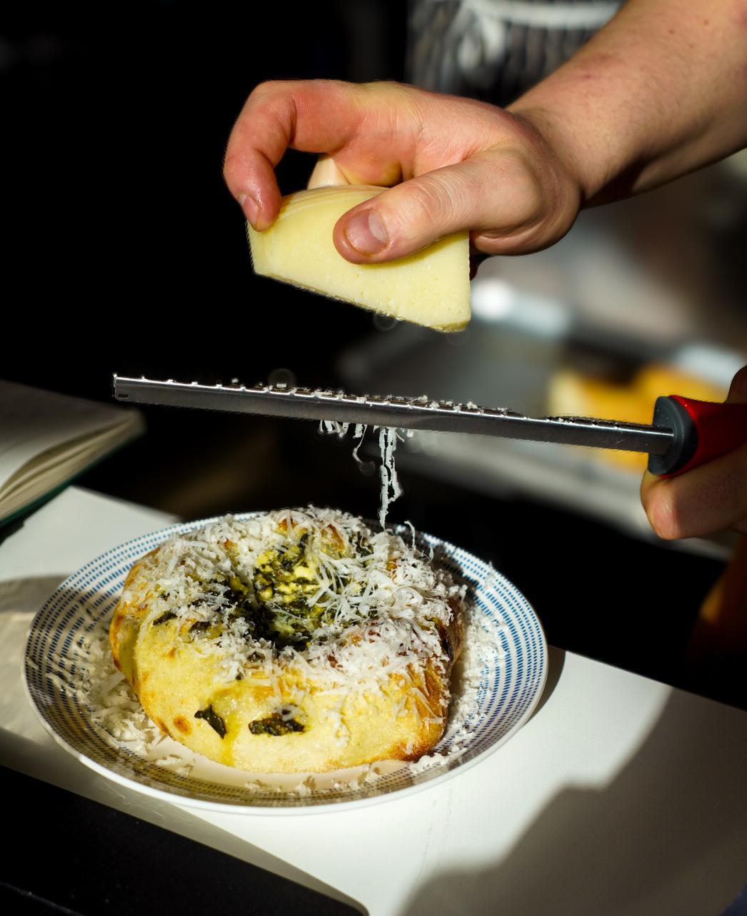 cheese being grated over spanakopita dish at kallos which has been added to the michelin guide