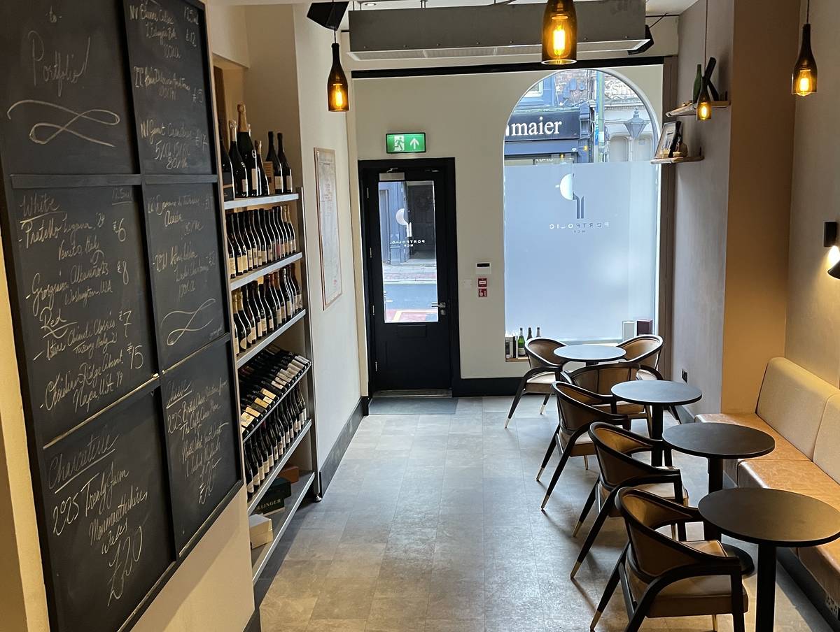 inside portfolio, table and chairs, wall with wine bottles and chalk board showing drinks menu