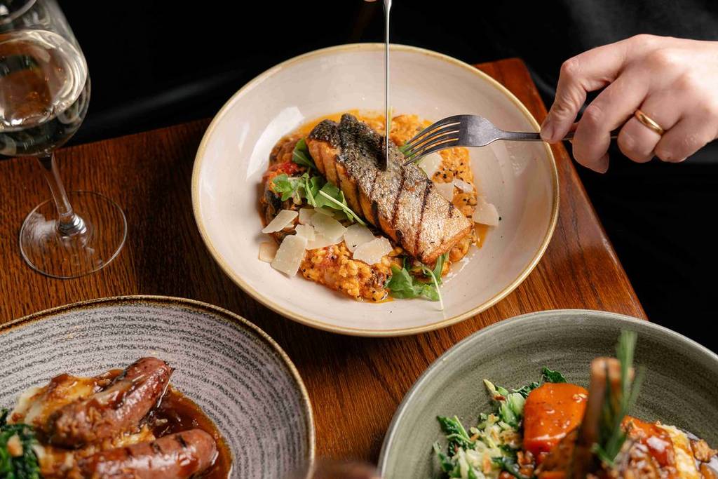 person cutting into salmon dish on table at almond family pub which is offering 2 for 1 mains during january as part of food offers in greater manchester