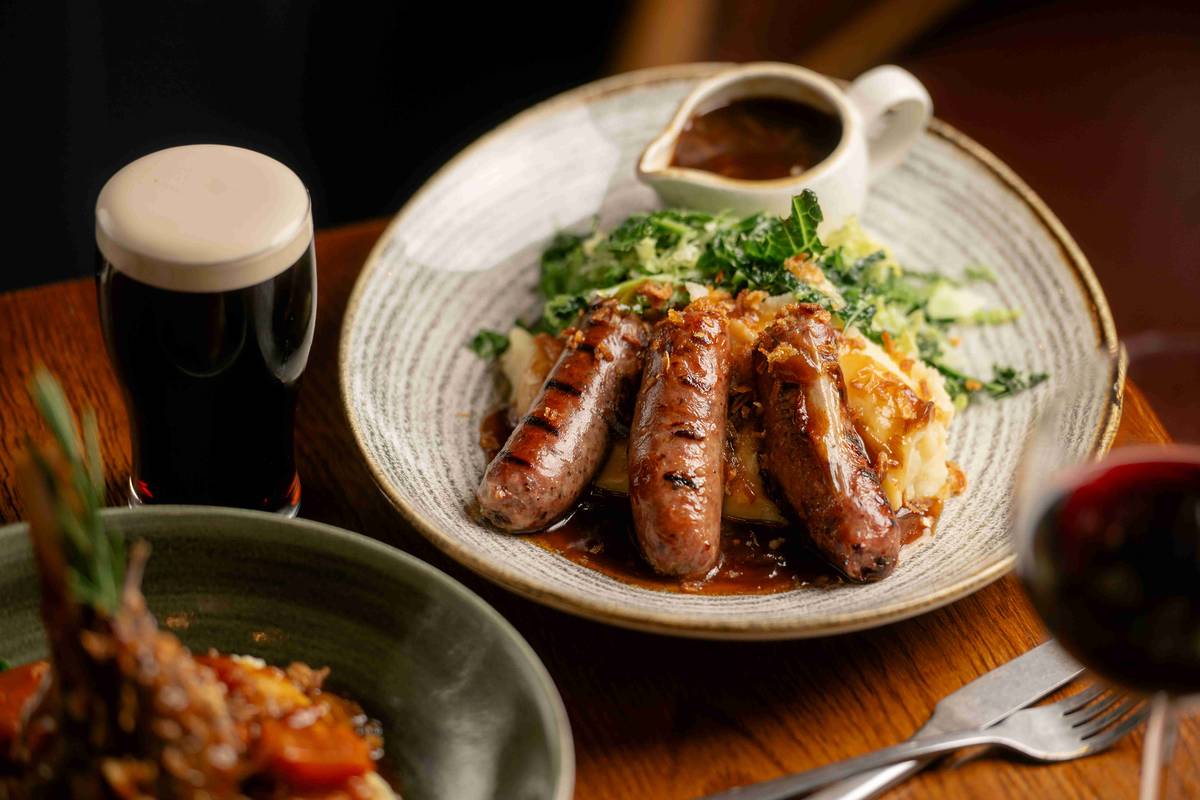 sausages and mash dish next to pint of stout and glass of red wine at almond family pub