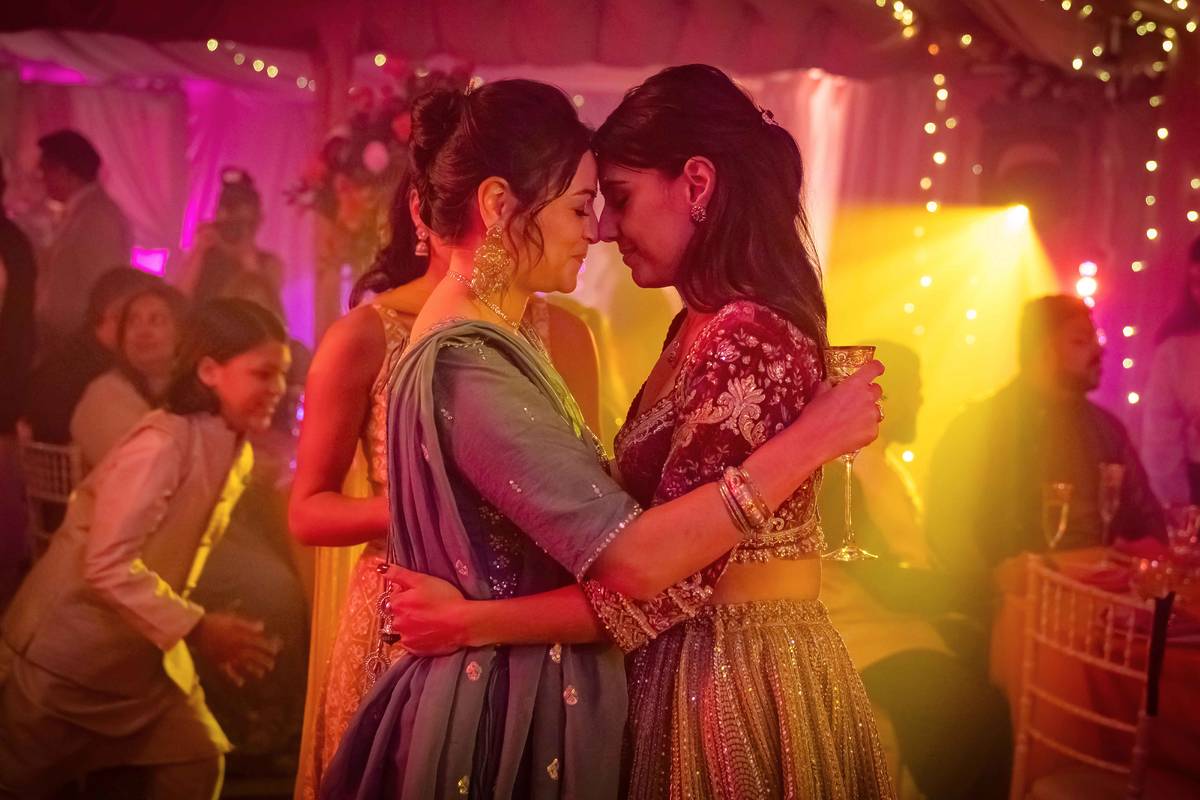two women dressed in saris with heads together at party