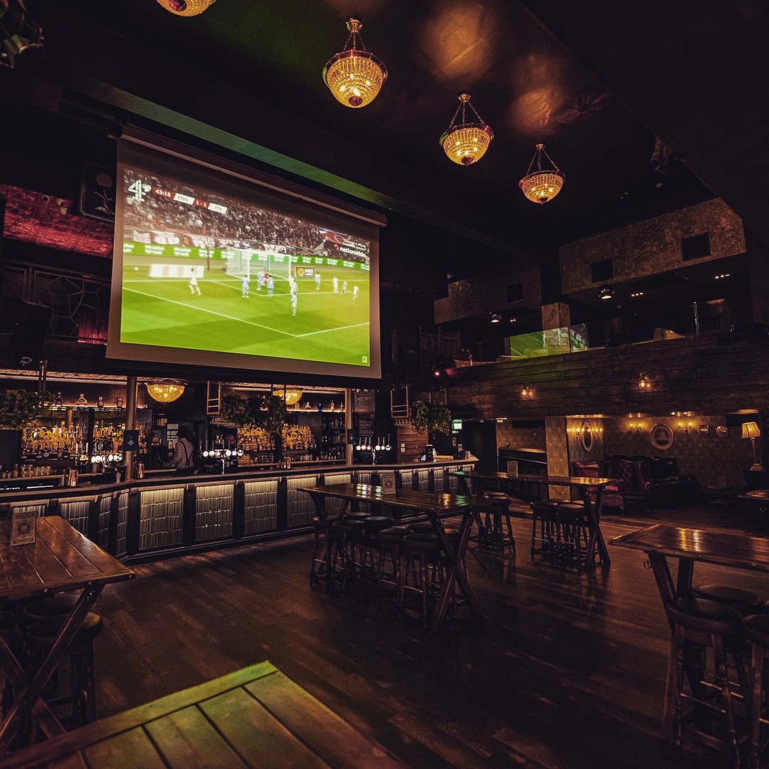 inside peaky blinders bar with football on big projector screen