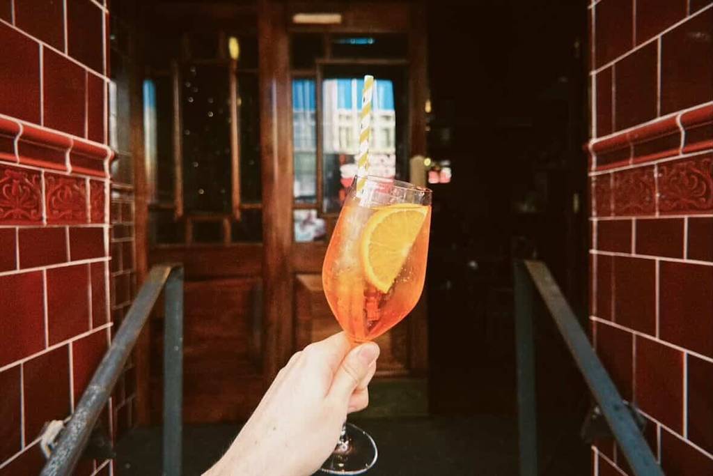a hand holding an aperol spritz in a doorway