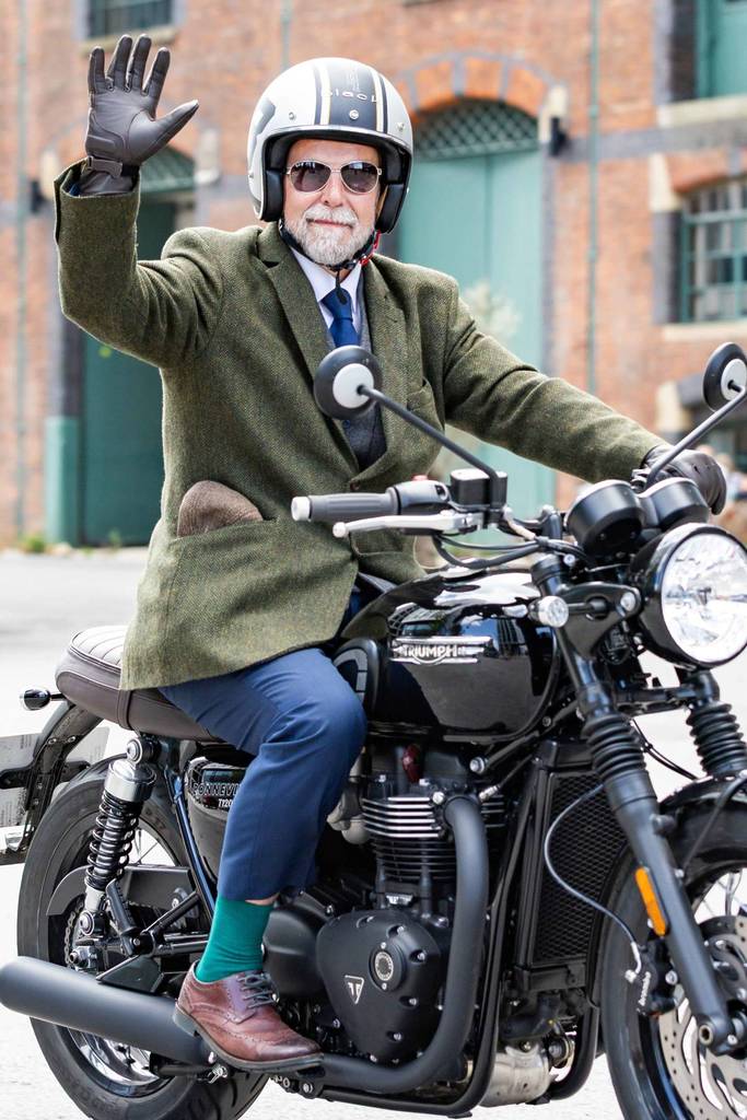 man dressed smart on motorbike waving as part of distinguished gentleman's ride in manchester