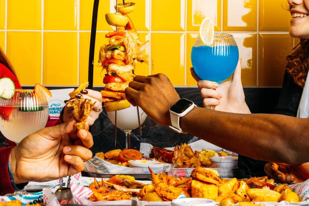person holding blue cocktail and taking from seafood kebab