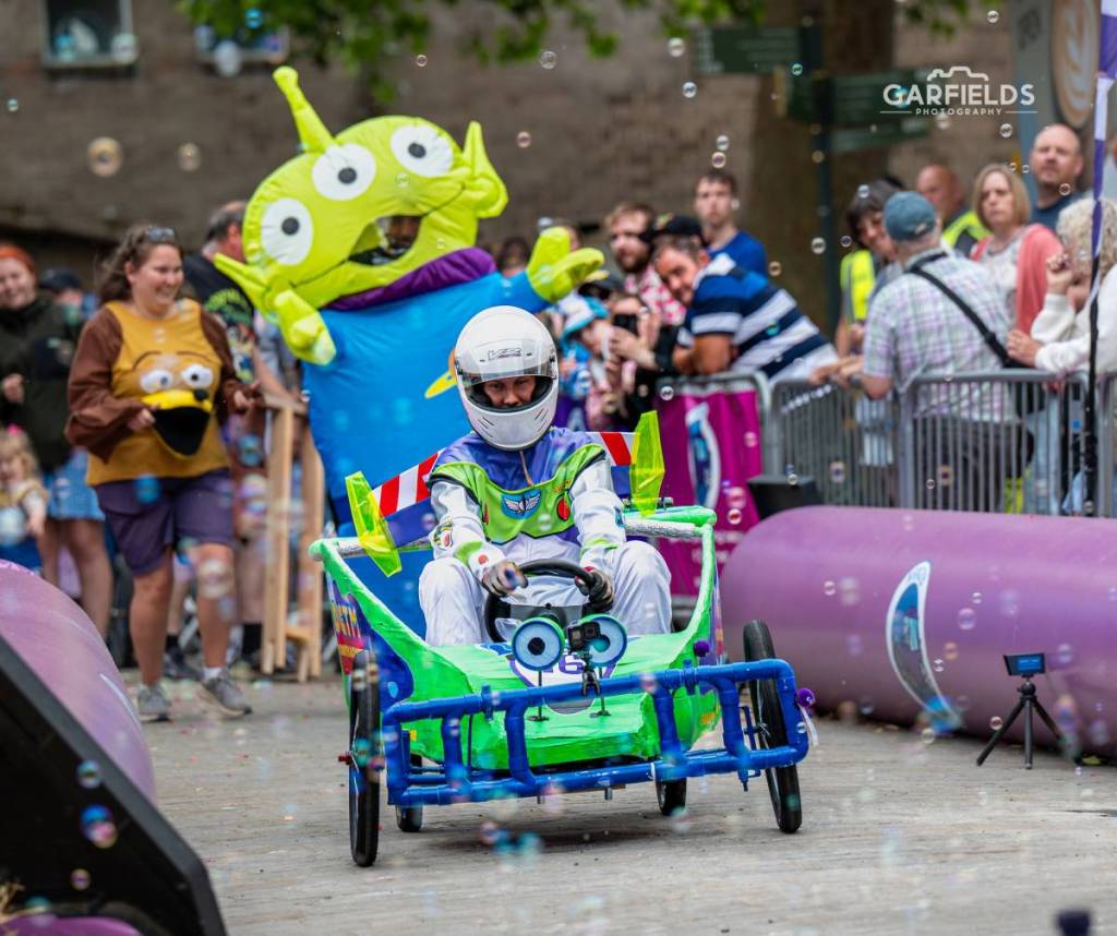 toy story-themed soapbox with inflatable alien behind driver