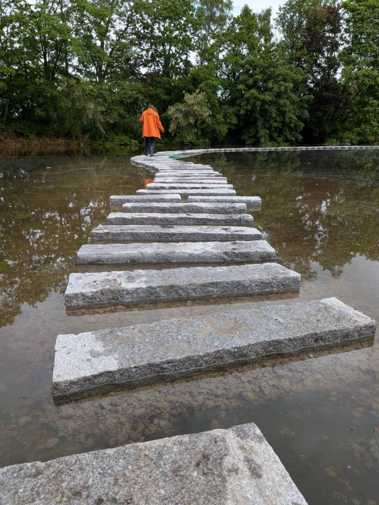 woman wearing orange coat walking along stepping stones at wwt martin mere