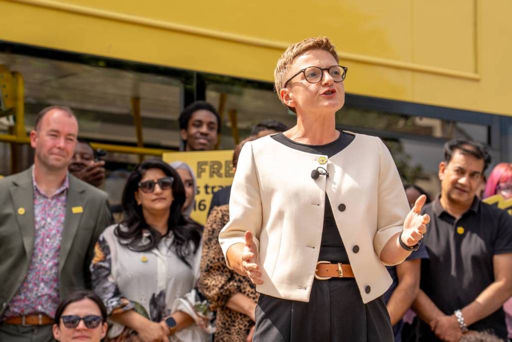 Bev Craig speaking in front of yellow bee network bus in Bolton