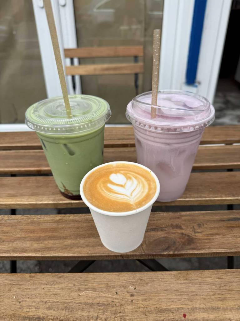 selection of drinks from 7zz including iced strawberry matcha, ube cold foam latte and a flat white at front on table