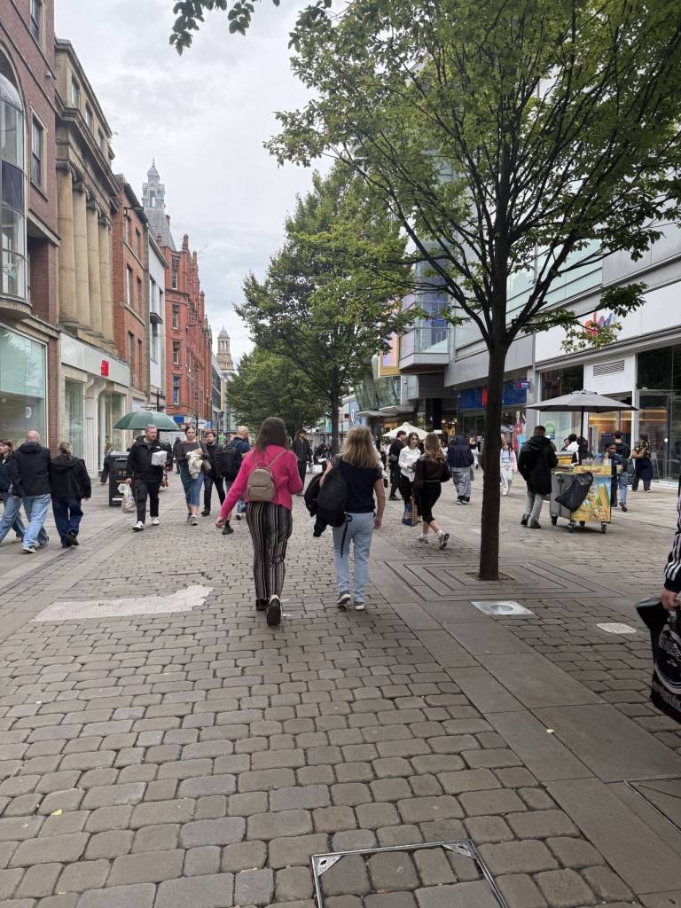 people walking down market street in manchester with stalls in background