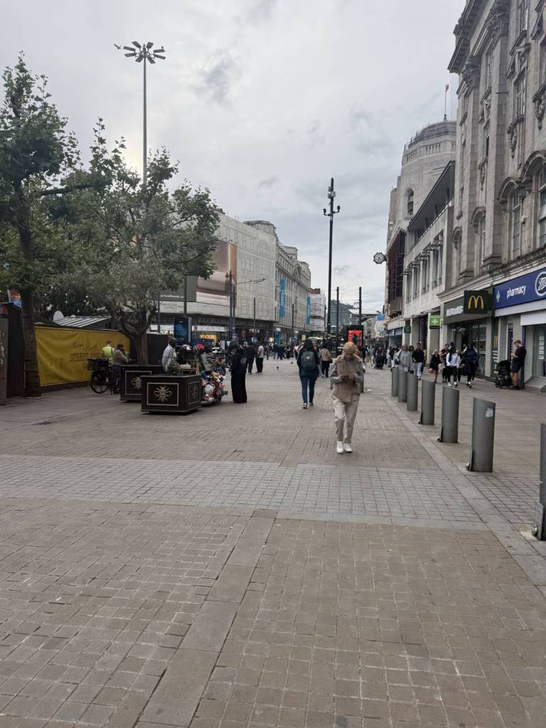 people walking past piccadilly gardens in manchester