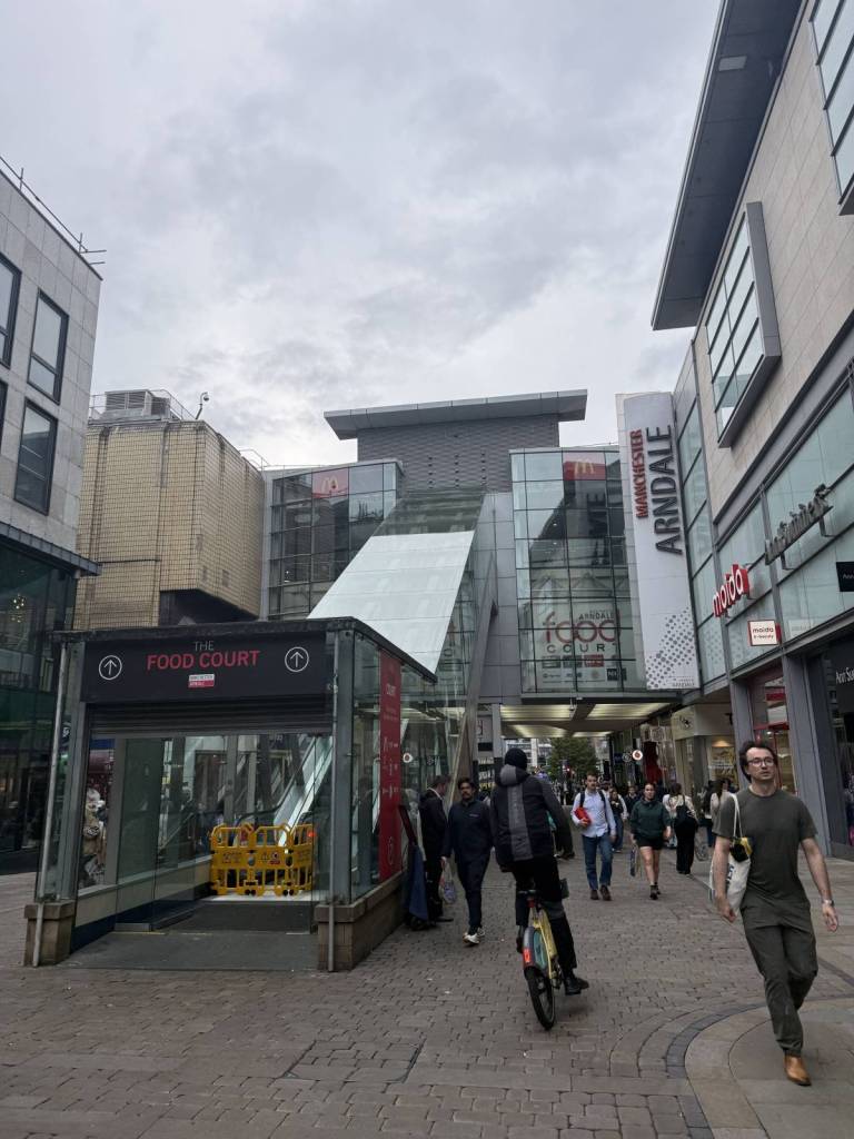 people walking and cycling past entrance to manchester arndale food court