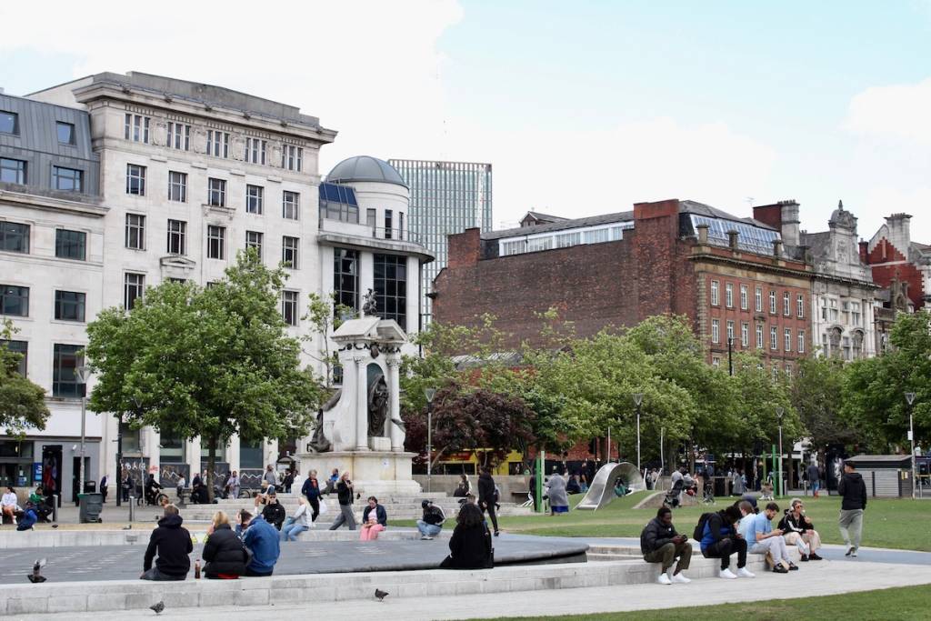 piccadilly gardens in manchester, people sit around the fountain