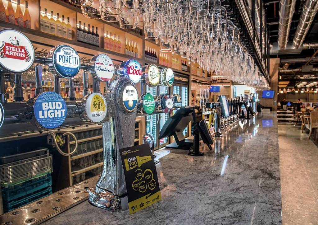 length of bar with multiple beer taps and glasses hung above