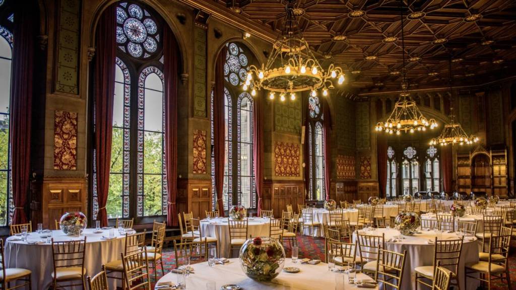 tables laid in banquet hall with stain glass windows behind and grand chandeliers hanging from ceiling