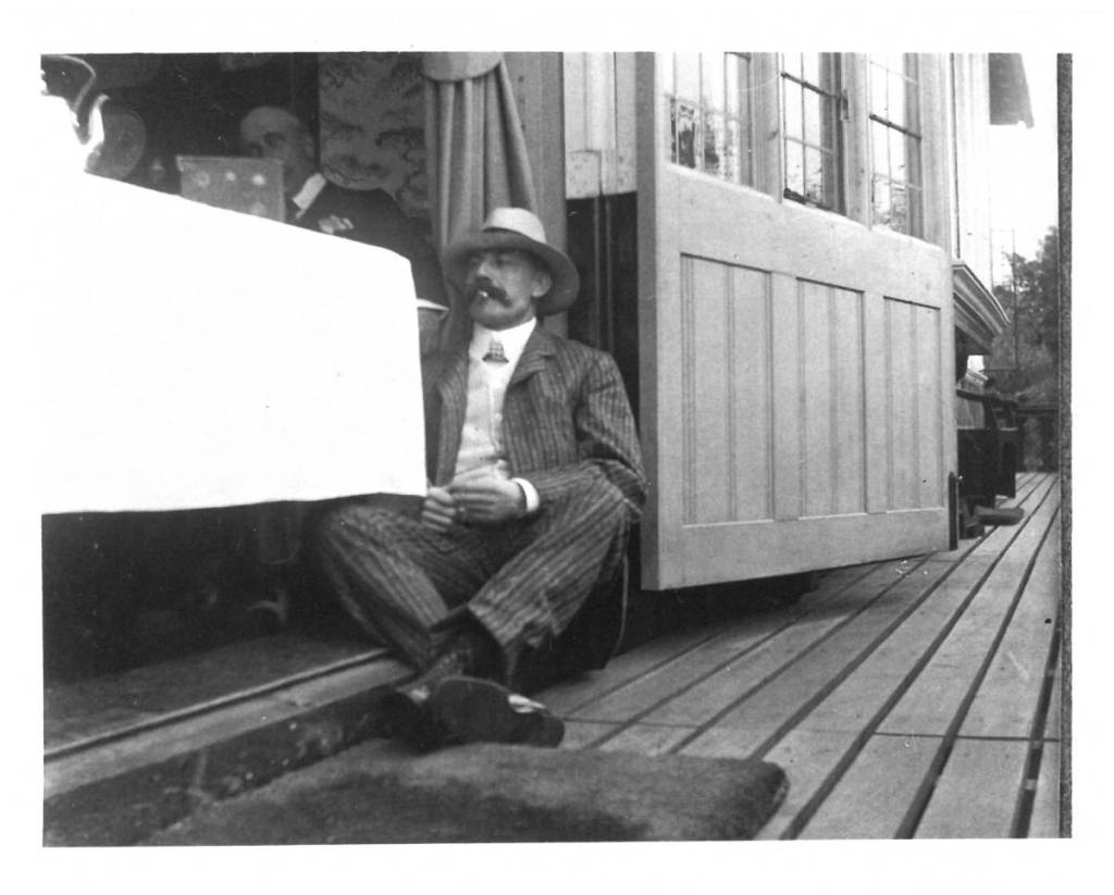 black and white photo of sir edward elgar sat down on wooden floor with boater hat on