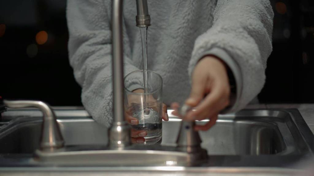 person with grey jumper running tap to fill glass with water
