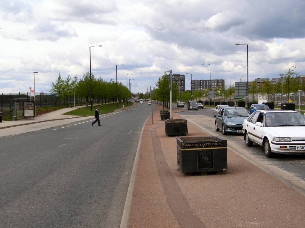 cars driving on alan turing way in manchester with person crossing road on left hand side