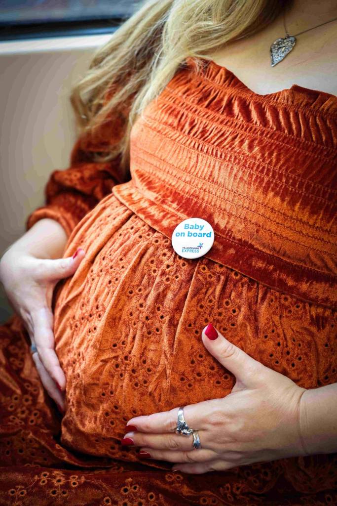 woman wearing orange dress holding baby bump with transpennine express baby on board badge on