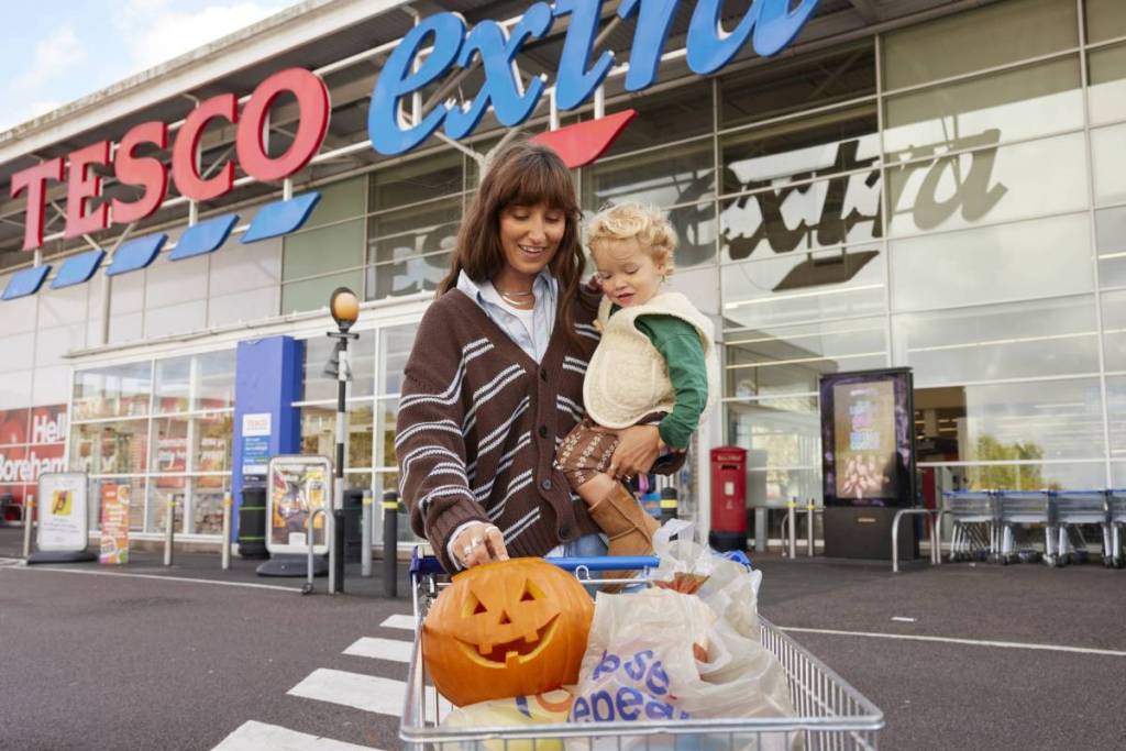 woman holding child with carved pumkin in trolley outside tesco extra supermarket