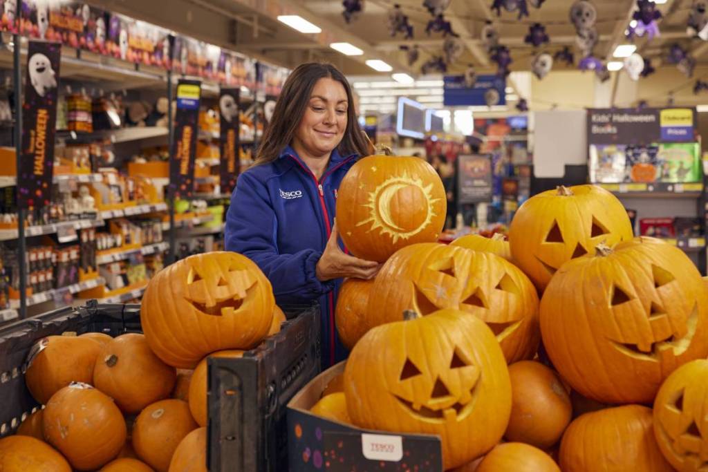 woman with tesco jumper holding carved pumpkin next to lots of carved pumpkins