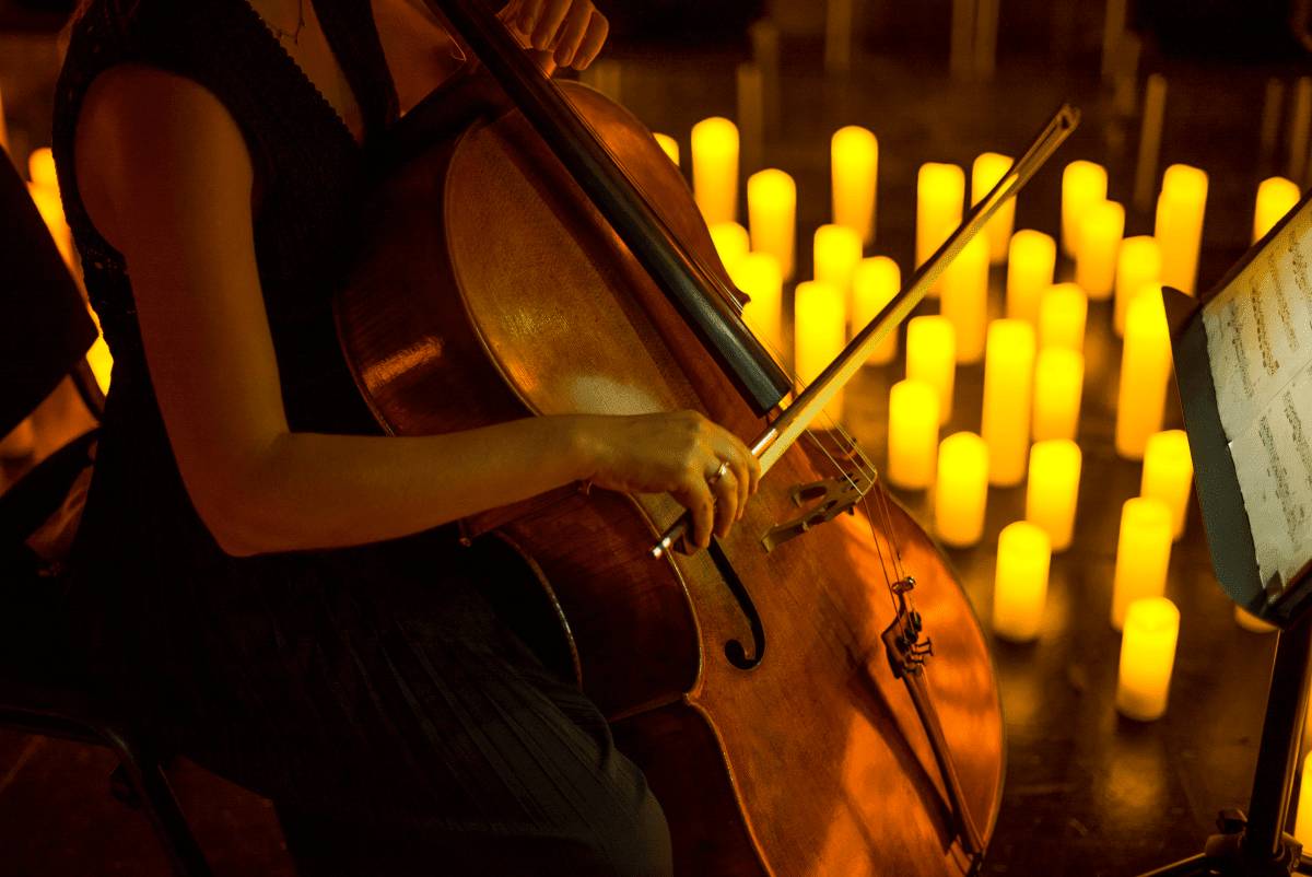 Primer plano de un violonchelista tocando sobre un escenario cubierto de velas durante un concierto Candlelight.