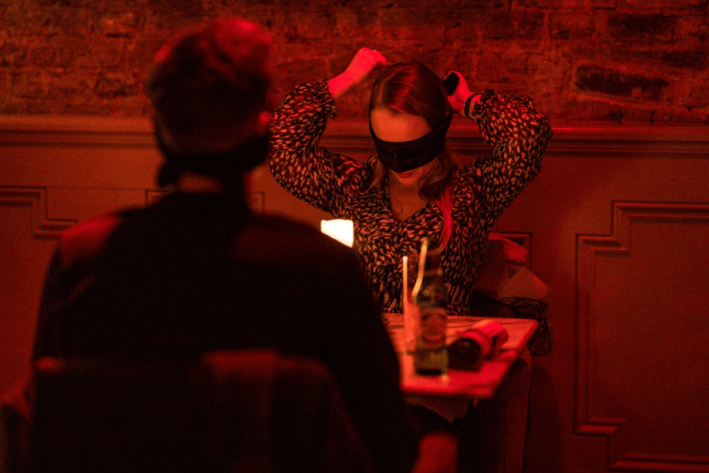 A woman fixing her blindfold while having dinner with a man at the Dining in the Dark experience.